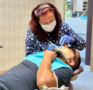 Dr. Manasovska working with a male patient during a dental cleaning with dental tools in his mouth