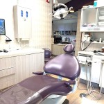A close-up of a dental operatory featuring a purple reclining chair, overhead clinical lighting, and a wall-mounted monitor for patient education.