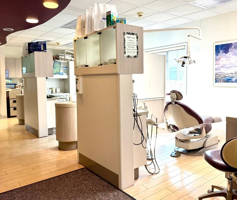 An open-concept dental clinic showing a modern treatment bay with a purple patient chair and organized medical storage units.
